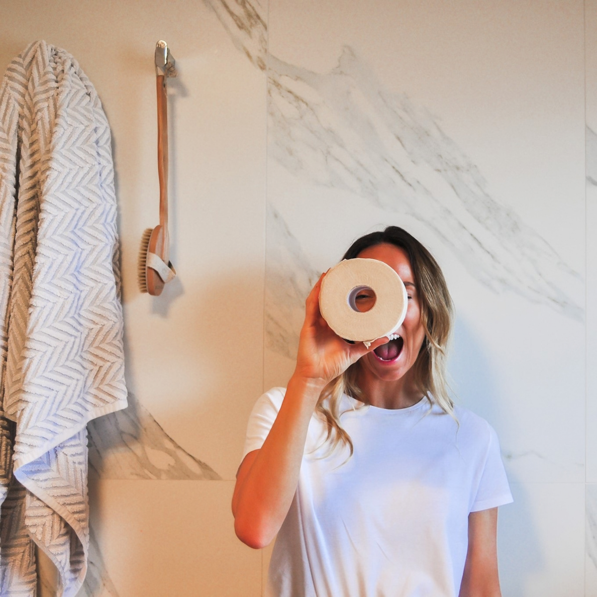 Person holding a roll of toilet paper in front of a mirror in a bathroom.