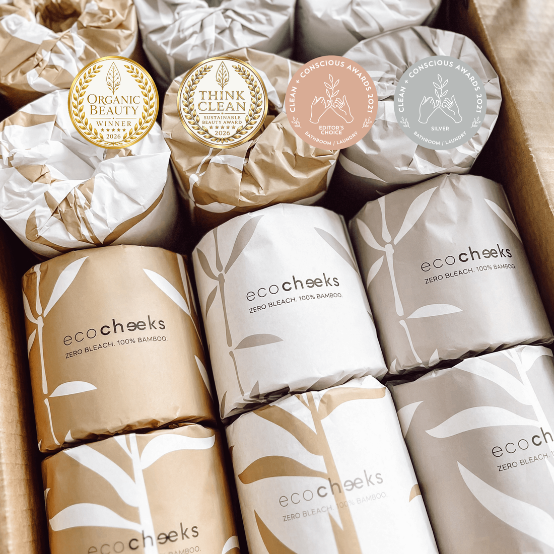 A box of eco:cheeks Zero Bleach 100% Bamboo Shampoos, showing multiple wrapped bottles in gold, white, and gray packaging with bamboo leaf patterns and award seals.